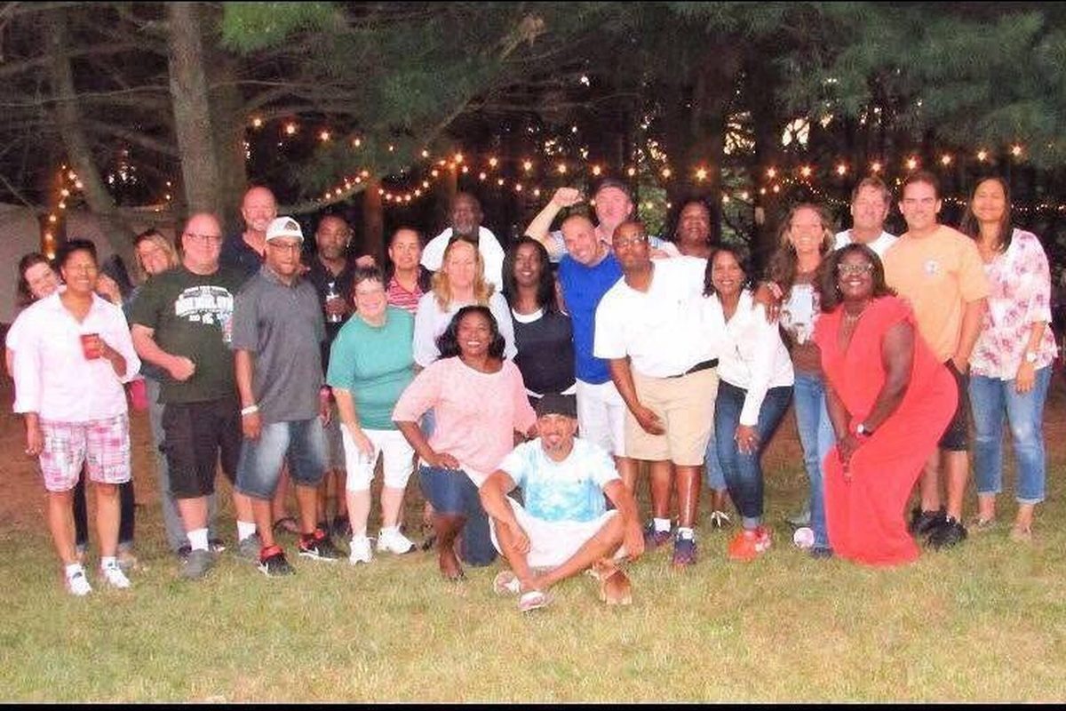Large group of classmates gathered outdoors under string lights at an evening reunion